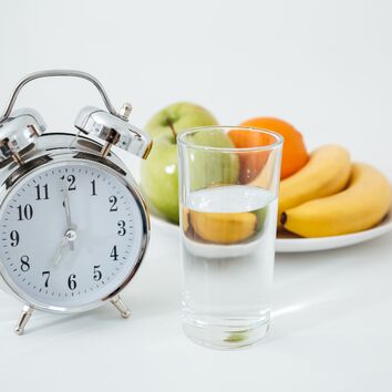 Wecker, Glas Wasser und ein Teller gefüllt mit Obst